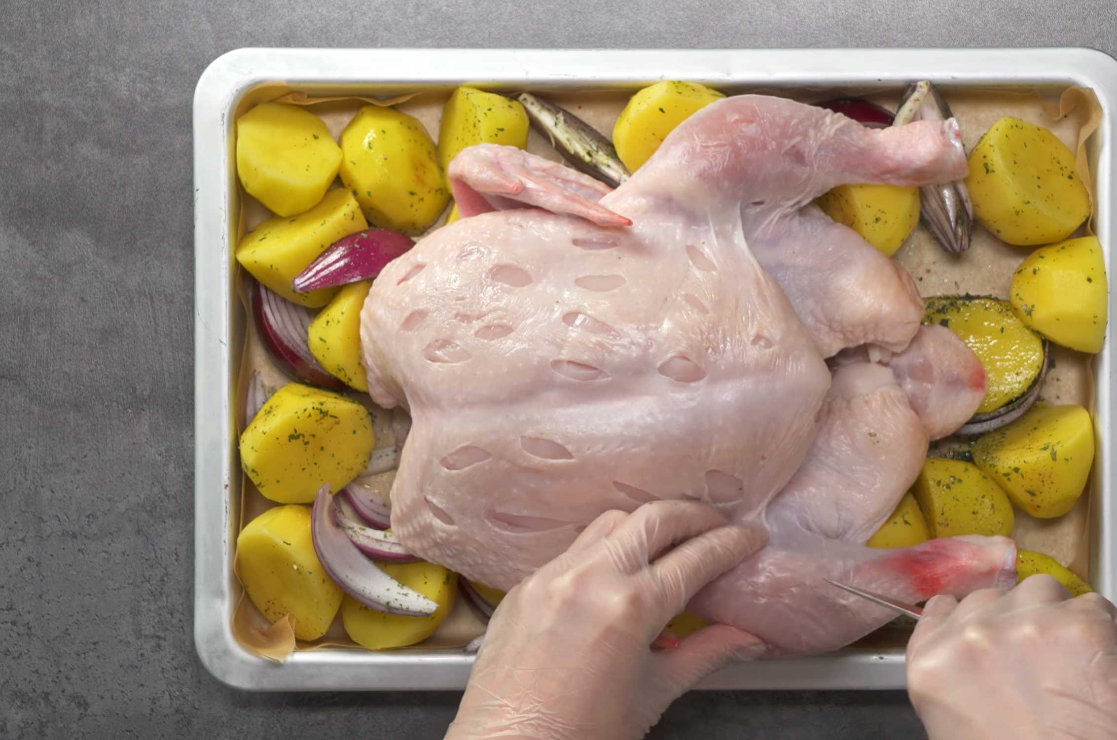 Возьмите тушку курицы и вытрите ее кожу бумажным полотенцем. Переложите курицу на противень. Возьмите некрупный нож и сделайте несколько отверстий на грудках и на ножках курицы. Курица с прованскими травами и картошкой-Шаг 5