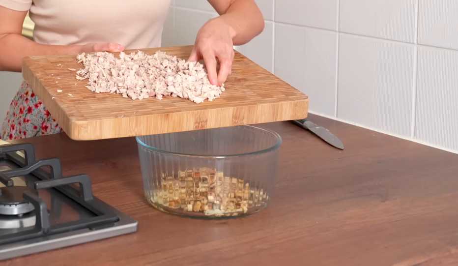 Добавьте курицу: Нарежьте куриное филе мелкими кубиками и добавьте к грибам и луку. Блинчики с курицей и грибами-Шаг 10