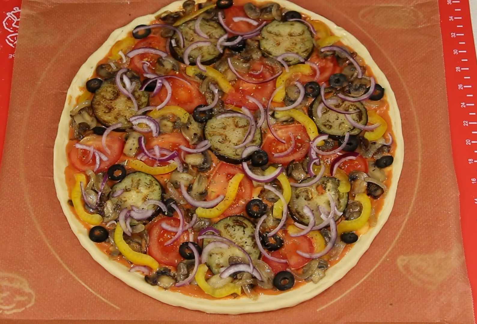 Соберите пиццу: на тесто равномерно нанесите соус, выложите баклажаны, помидоры, грибы с луком, перец, красный лук и маслины. Уложите всё плотно, но без перегруза. Веганская пицца с овощами-Шаг 10